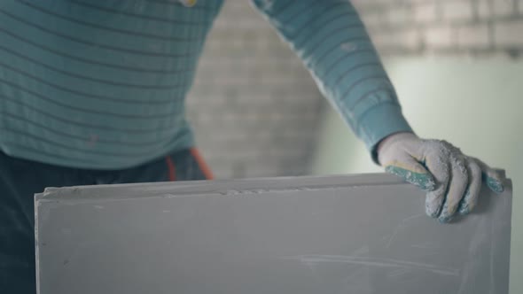 Worker Holds Gypsum Plasterboard and Beats with Hammer