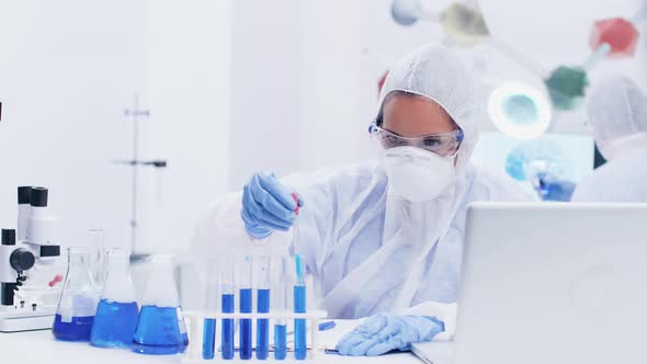 Female Scientist in Modern Laboratory Wearing a Coverall Equipment Taking Samples of Blue Liquid