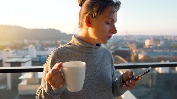 Woman Starts Her Day with a Cup of Tea or Coffee and Checking Emails in Her Smartphone on the