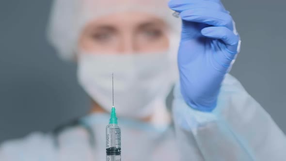 Young Woman in Coat Cap and Mask Holds Syringe Releasing Air