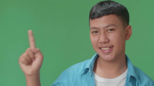 Inspired Young Asian Boy Smile And Pointing To The Side While Standing In The Green Screen Studio