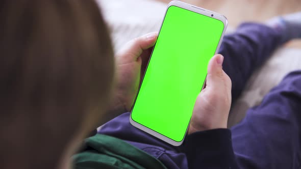 The Child Is Holding a Smartphone in Hand with a Green Screen for Keying Playing a Game