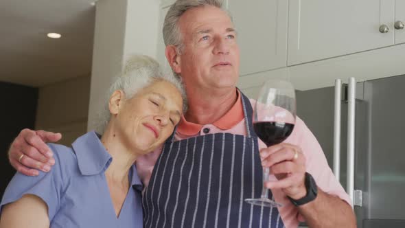 Animation of happy caucasian senior couple wearing aprons embracing and drinking wine