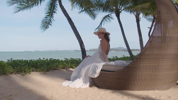 Woman in Dress Seats on the Beach Loge During Sunset Camera Moves Away From Her