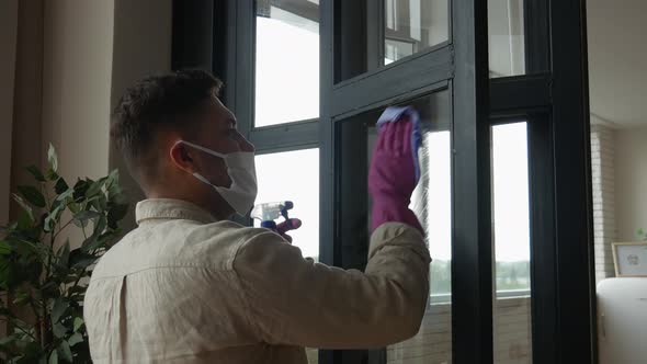 Concentrated young man in a protective mask applies spray to wash windows