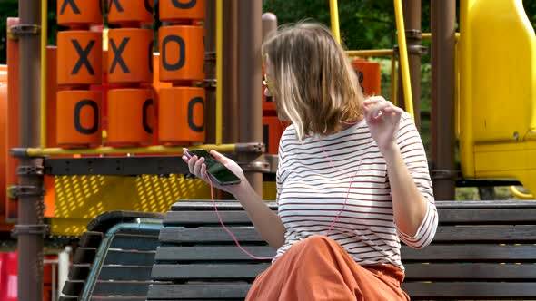 Young Beautiful Woman Listens To Music By Headphones and Smartphone