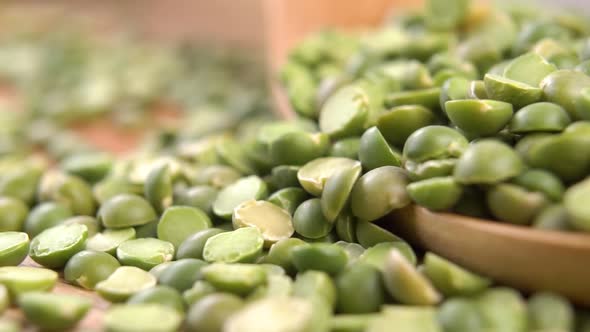 Dried split green peas fall on a pile in a wooden spoon on a wood surface