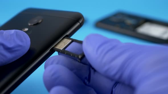 Hand in Blue Gloves Installs SIM Card in Black Smart Phone