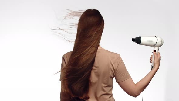 Woman Stands and Dries Head with Hairdryer Which Inflates Hair on White Background in Studio Back