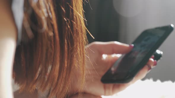 Young Woman Sitting on the Bed and Makes Online Shopping on a Smartphone. Online Shopping Concept.