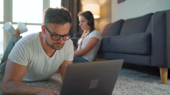 Couple Spends Time Together in a Cozy Room: Man Lies on a Carpet and Uses a Laptop, Woman with