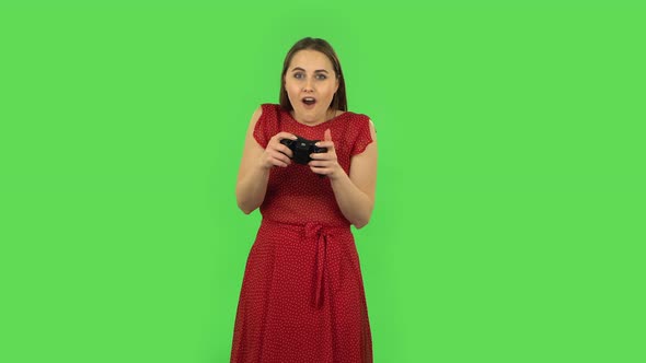 Tender Girl in Red Dress Is Playing a Video Game Using a Wireless Controller and Loses. Green Screen