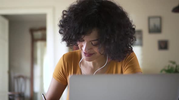 Young Black College Student Listening to Online Lesson and Writing Notes in Notebook Spbd