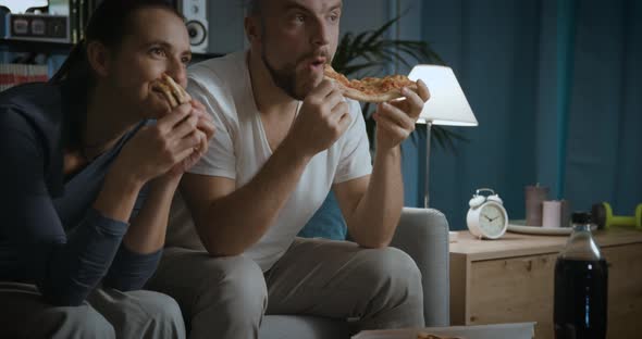 Happy couple sitting on the couch and eating pizza