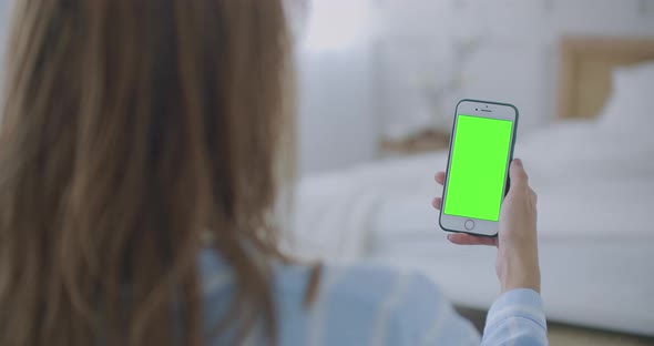 Woman Using and Looking Smart Phone Green Screen at Home. Young Girl Is Holding Smartphone With