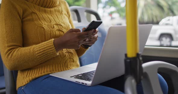 African american businesswoman with face mask using smartphone and sitting in bus