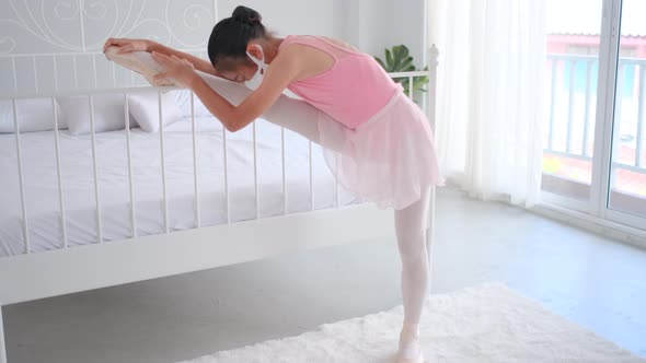 Asian ballet girl with pink dress and hygiene mask raise leg on bed before practice the dancing