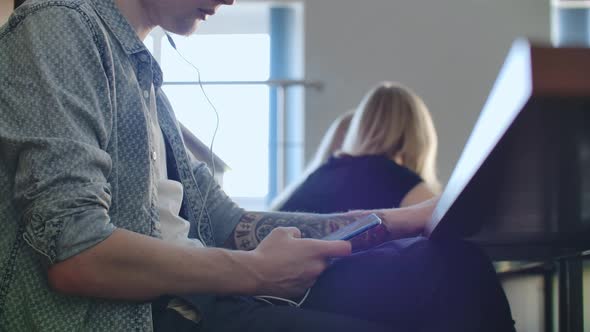 A Male Student in a University Auditorium Listens to Music in White Headphones During a Break