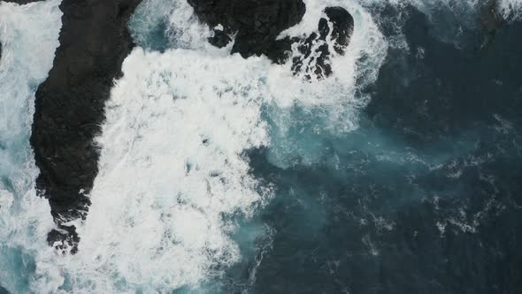 Aerial view of the crispy waves breaking on the rocks.