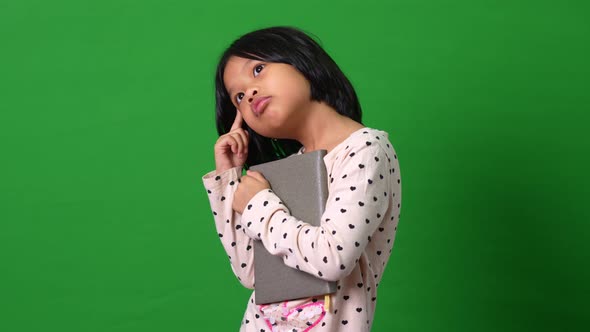 Portrait of cute Asian schoolgirl child 7-8 years looking at camera standing and holding book on the