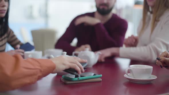 Close-up of Group of Unrecognizable People Putting Smartphones on the Table in Cafe. Friends