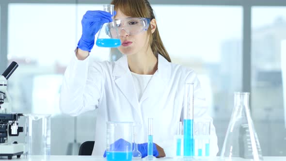 Female Research Scientist Looking at Blue Solution in Flask in Laboratory