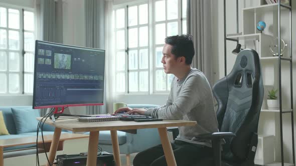 Asian Video Editor Man Using Desktop Computer For Editing Video While Working At Home