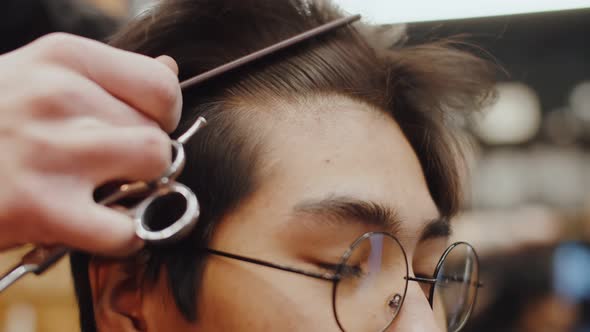 Barber's Hands Comb the Hair of an Asian Guy with Glasses Closeup