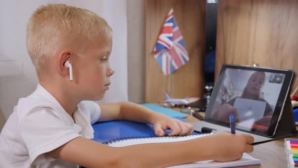 A Boy in Wireless Headphones Communicates in a Video Conference with a Teacher