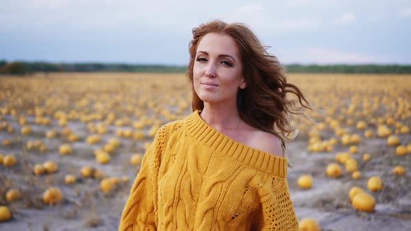 Young Smiling Woman Holding Pumpkin in Her Hands and Looking at Camera While Standing in Field
