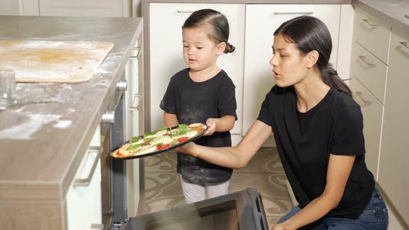 Little Girl Helps Mom Put Delicious Pizza Into Modern Oven