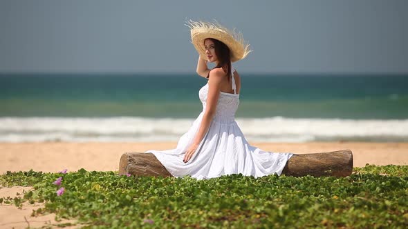 Woman in white dress sits on ocean beach