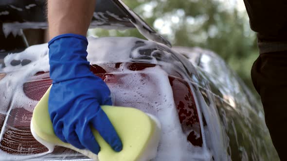 Close Up of a Male Hand in a Blue Glove with a Foam Rubber Sponge for Washing the Headlights