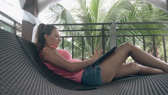 Girl Lies on Curved Sunbed and Types on Laptop Keyboard