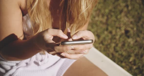 Blond Woman Texting On Smartphone In Sunny Garden
