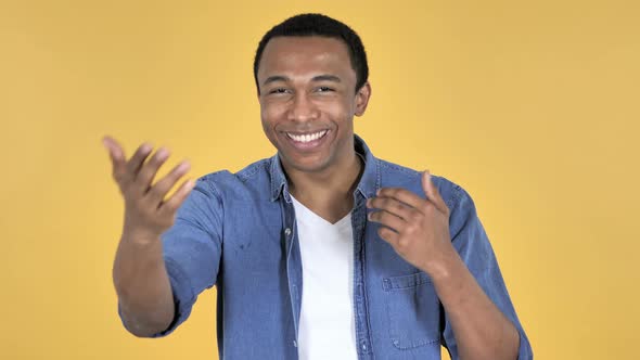 Young African Man Inviting Customers with Both Hands, Yellow Background