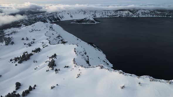 Drone shot of snowy shores of volcanic caldera lake, Crater Lake, Oregon, USA