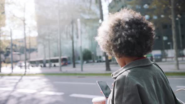 Back view of African woman texting by phone while walking