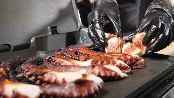 Grilling Octopus Tentacles with Sliced Figs. Close-up Shot of Chef Hands Putting Juicy Figs Onto