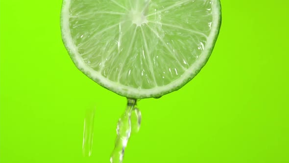 Water falling from green hue lime on green background. Lime slice and water splashing, drops