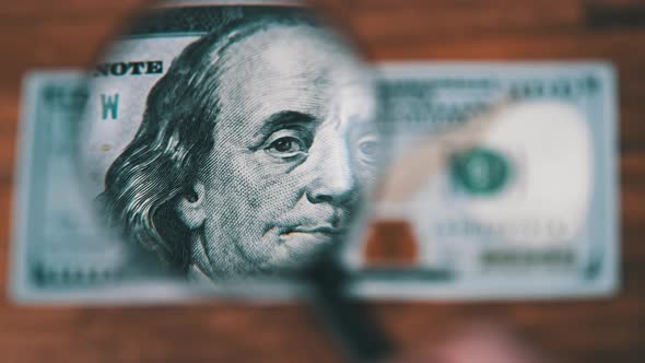 One Hundred Dollars Look Under Magnifying Glass on Wooden Table