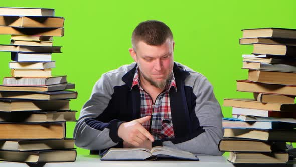 Man Sitting at Table with Books and Reading an Interesting Chapter. Green Screen