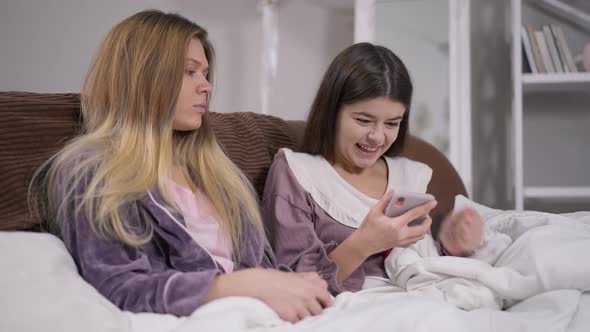 Excited Young Charming Woman Rejoicing Reading Message on Smartphone at Pajama Party with Friend