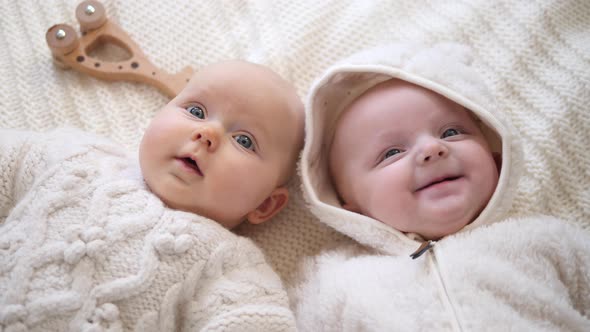 Twins Lying Together. Baby Girls Wearing Knitted Sweaters Playing With Eco Wooden Toys. 