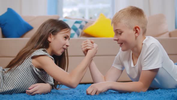 Happy Boy and His Sister Arm Wrestling Laying on the Floor in Living Room