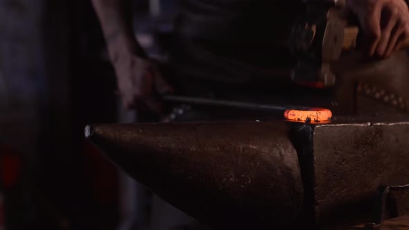 Focused young blacksmith heating and striking metal on anvil in workshop