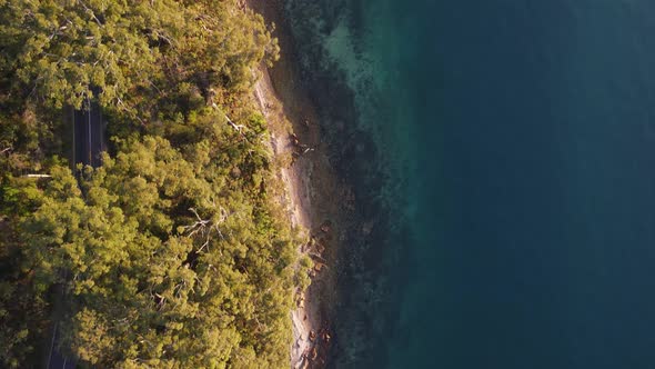 High drone view following a remote road way winding through a coastal headland next to a tropical re