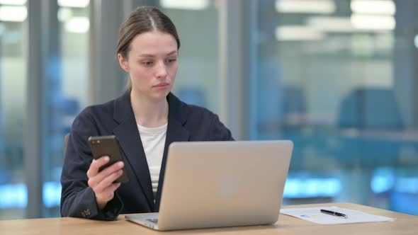 Young Businesswoman Working on Smartphone and Laptop in Office