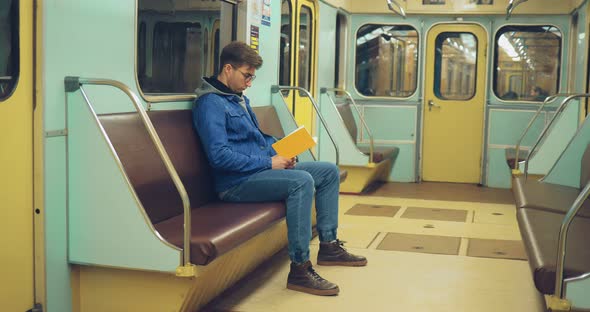 Young Man with Glasses is Reading a Book in an Empty Subway Car
