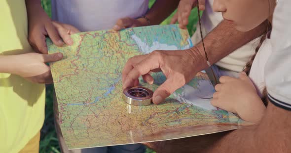 Close Up of Old Man Using Compass Searching Route with Children Looking Standing Holding Map